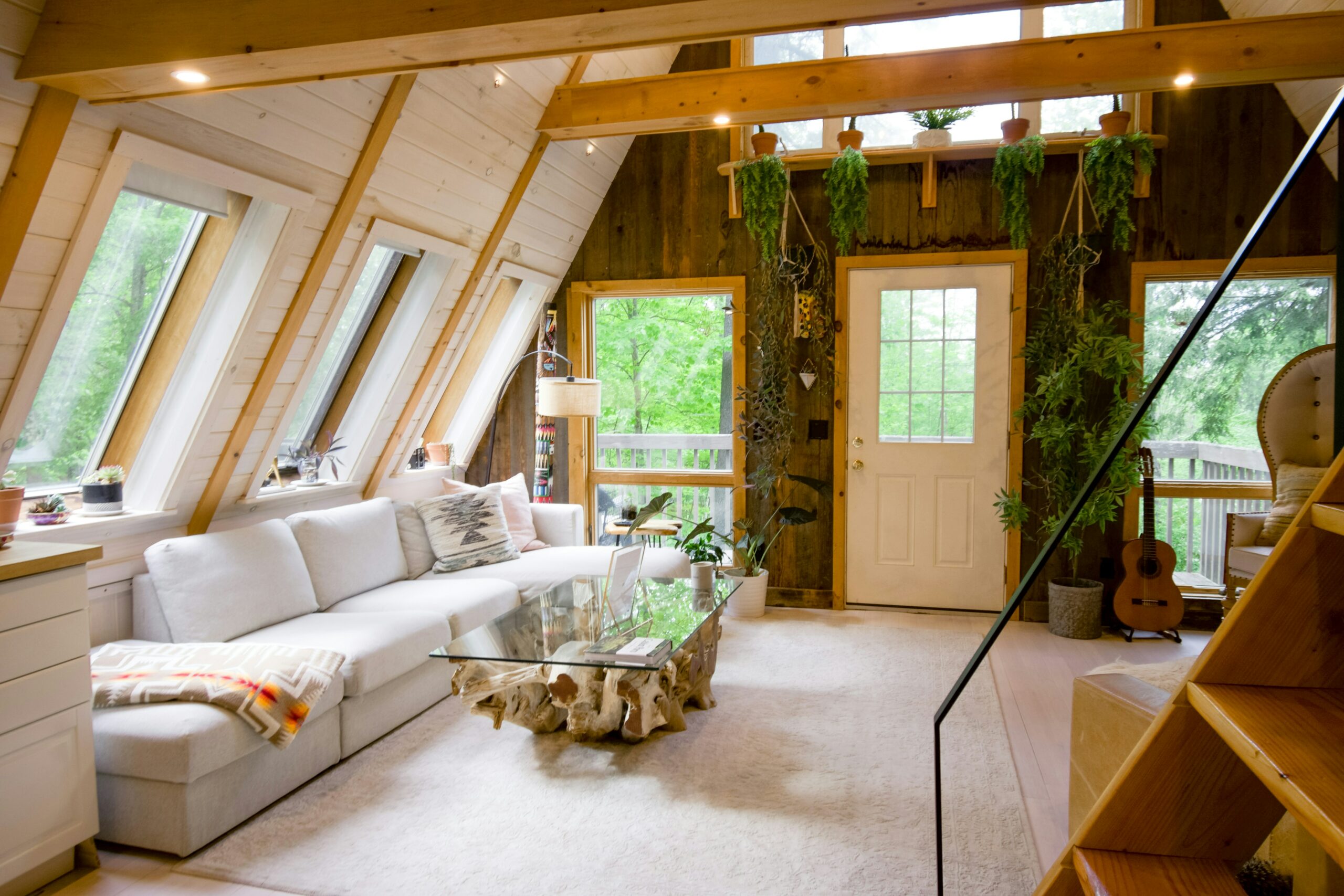 Valoisa huone, jossa on viistot kattoikkunat, valkoinen sohva, lasinen sohvapöytä ja runsaasti viherkasveja.